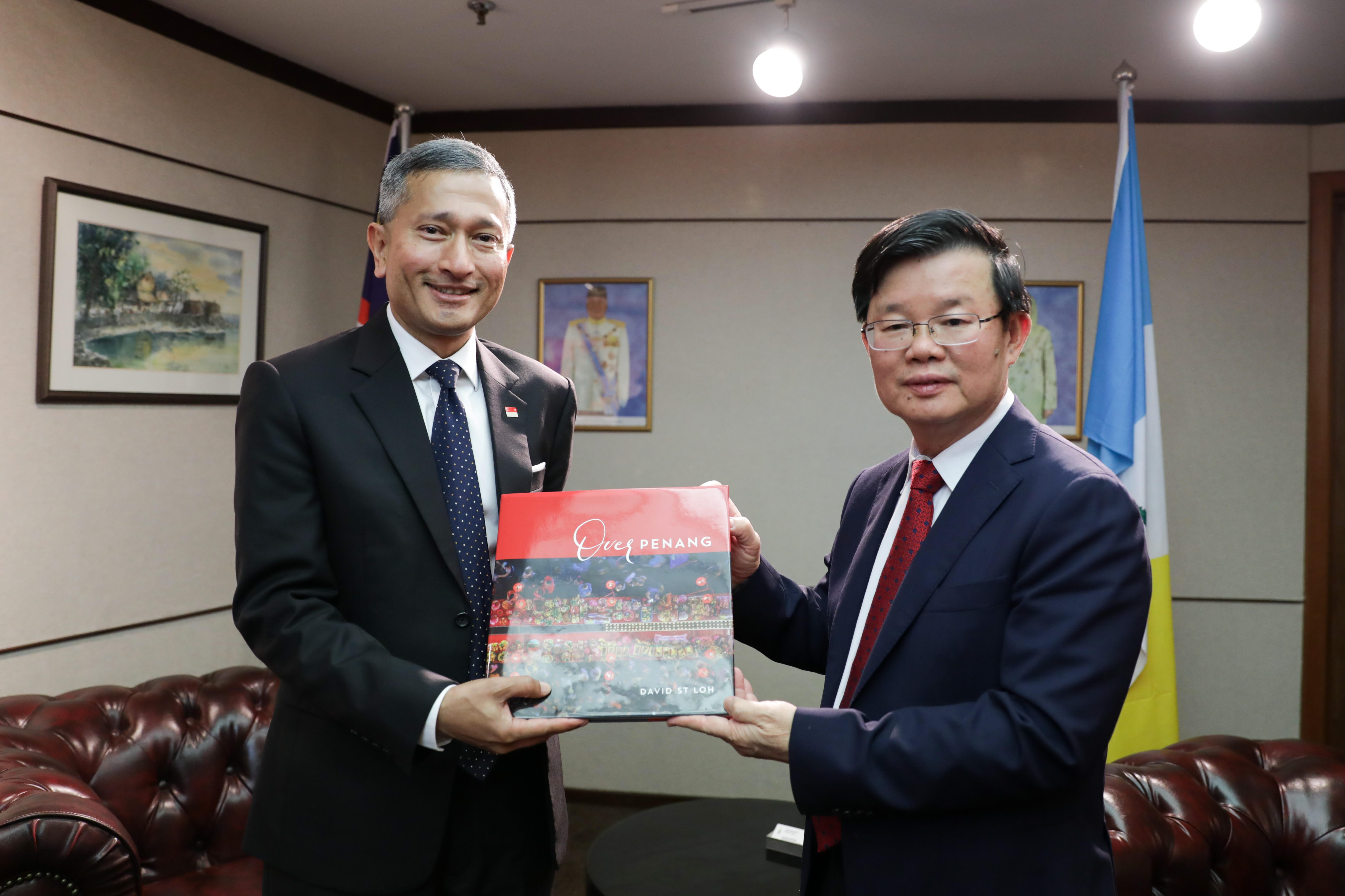 Two men in suits holding the book "Over Penang" by David ST Loh in an office.